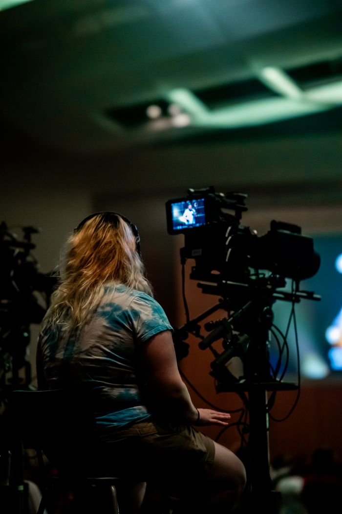Back view of a woman camera operator working at an indoor event.