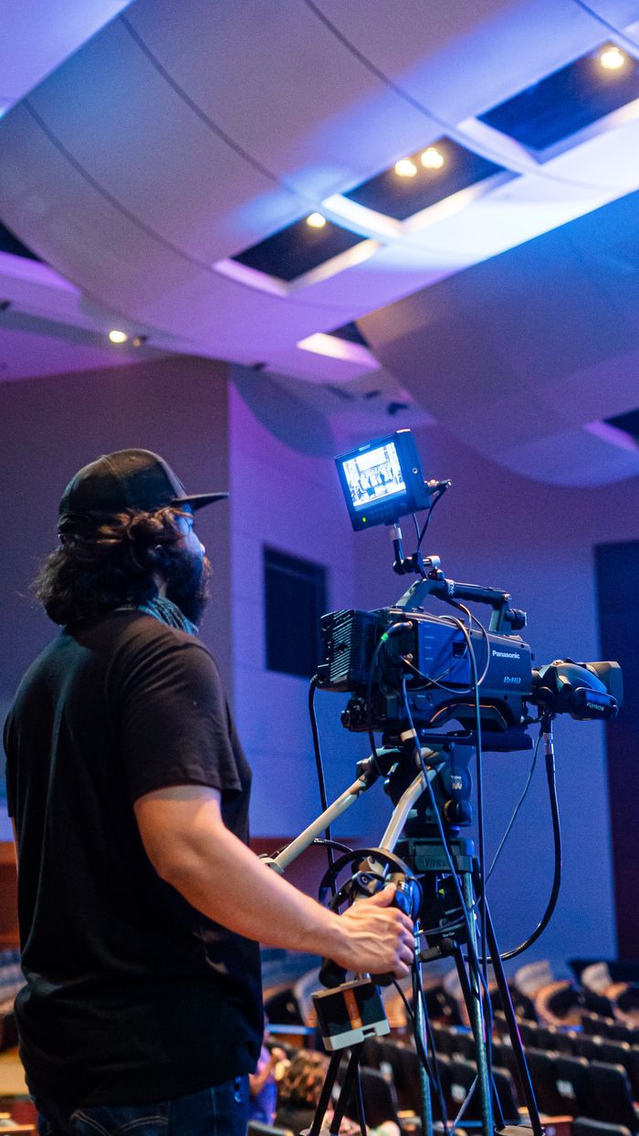 Back view of bearded camera man recording stage during music performance in illuminated concert hall