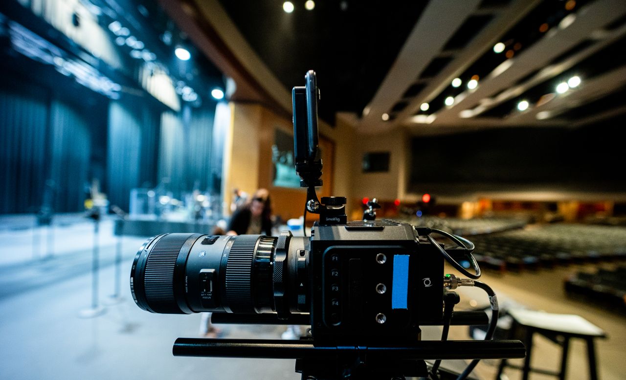 Contemporary professional video camera with lens placed on tripod near stage under ceiling with lights in studio